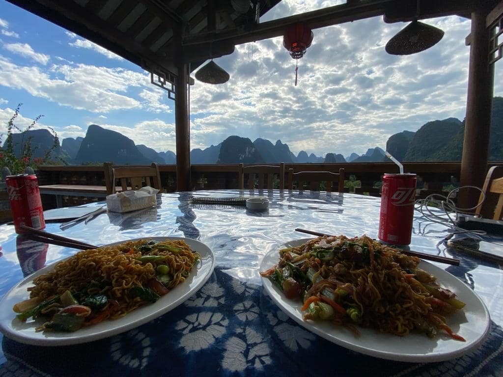 Plats de fideus xinesos servits a la terrassa del Riverside Retreat Hotel amb vistes a les muntanyes il·luminades de Yangshuo