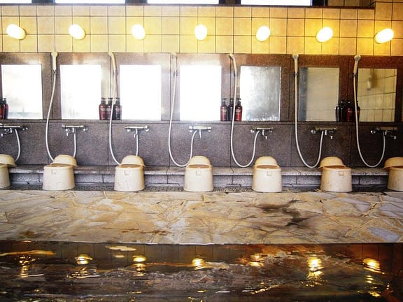 Interior d’un onsen de fusta amb vapor suau i llum tènue entrant per les finestres
