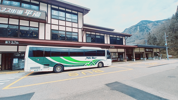 Bus aturat davant de l’entrada d’un onsen de muntanya, amb l’edifici de fusta i el vapor sortint de les termes.