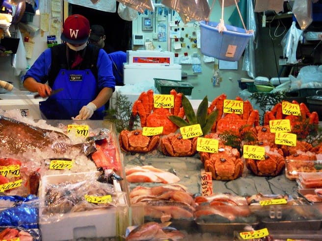 Parada del mercat de Tsukiji amb peix fresc exposat i venedors preparant el gènere al matí.