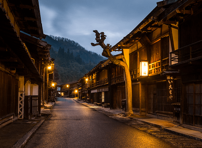 Carrer principal de Tsumago de nit, il·luminat suaument per llanternes i envoltat de cases de fusta tradicionals.
