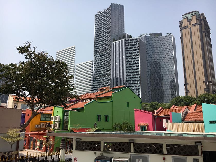 Cases tradicionals de colors davant de gratacels moderns a Singapur, símbol del contrast urbà durant un viatge cultural