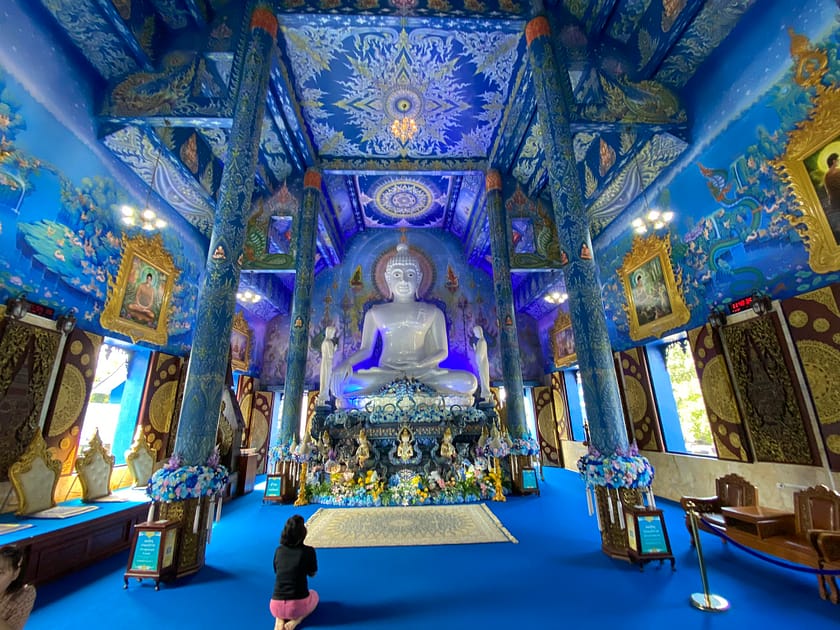 Interior del Temple Blau de Chiang Rai amb l’estàtua blanca de Buda envoltada de murals blaus i daurats
