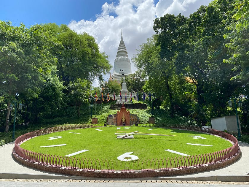 Parc del Wat Phnom amb estupa blanca i rellotge floral – Un dia a Phnom Penh