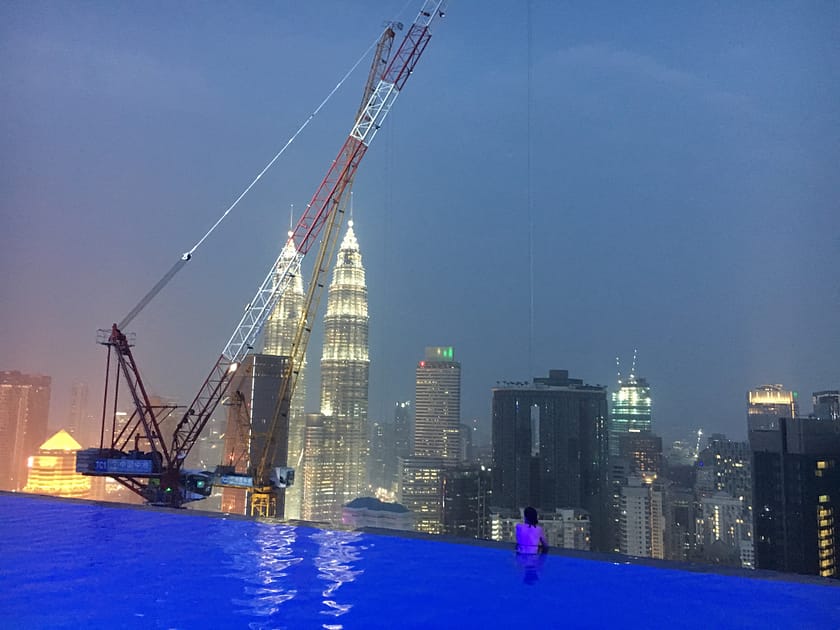 Vista nocturna de les Torres Petronas amb les llums enceses i una infinity pool en primer pla, durant una ruta per Kuala Lumpur en un dia