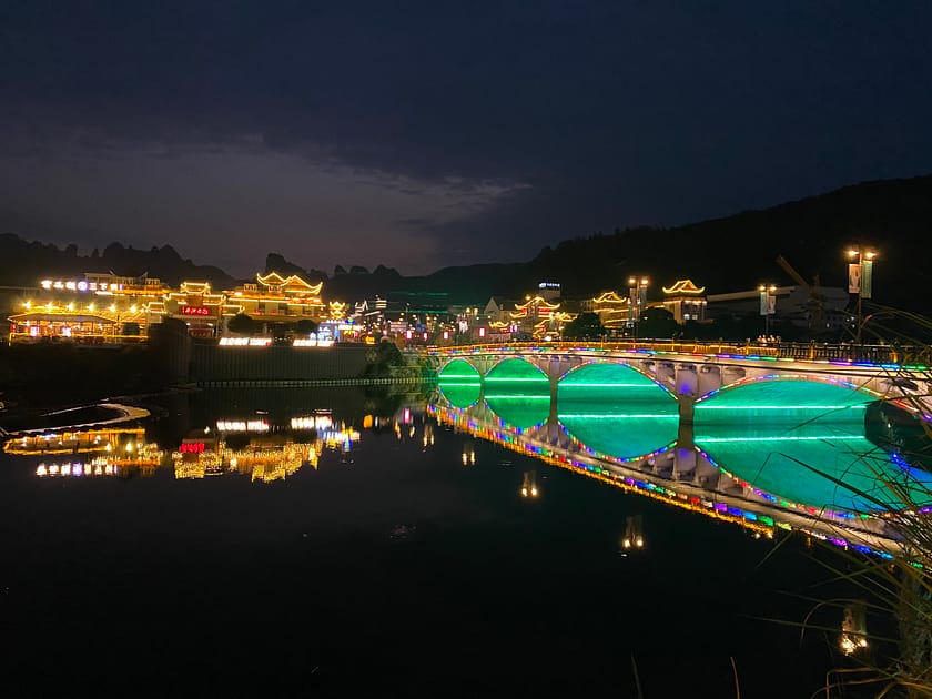 Vista nocturna de Wulingyuan amb llums suaus, edificis tradicionals i siluetes de muntanyes al fons