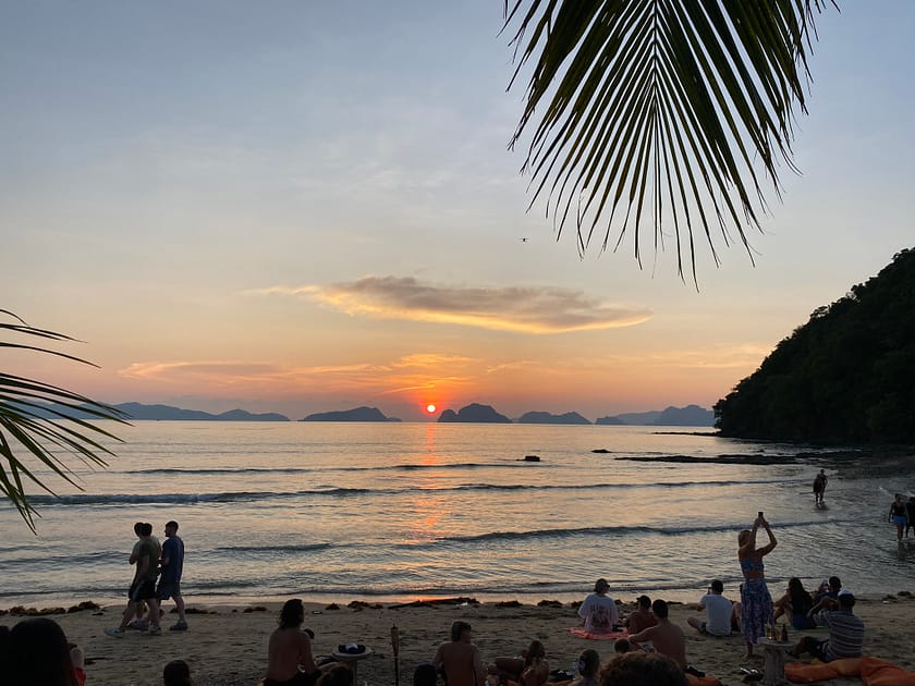 Posta de sol daurada a Las Cabañas Beach durant l’island hopping a El Nido, amb siluetes de palmeres i mar tranquil.