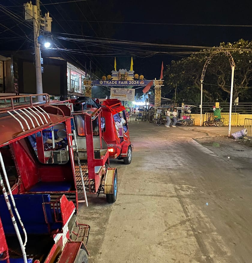 Carrer de Santa Fe a Bantayan de nit amb tuktuks i rètol de Trade Fair 2024, escenari típic per qui descobreix com anar a Bantayan